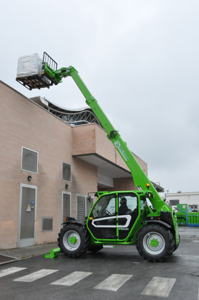 Merlo P30.10, stabilised telehandler, fully extended boom with a pallet attached on pallet forks, reaching above a building.