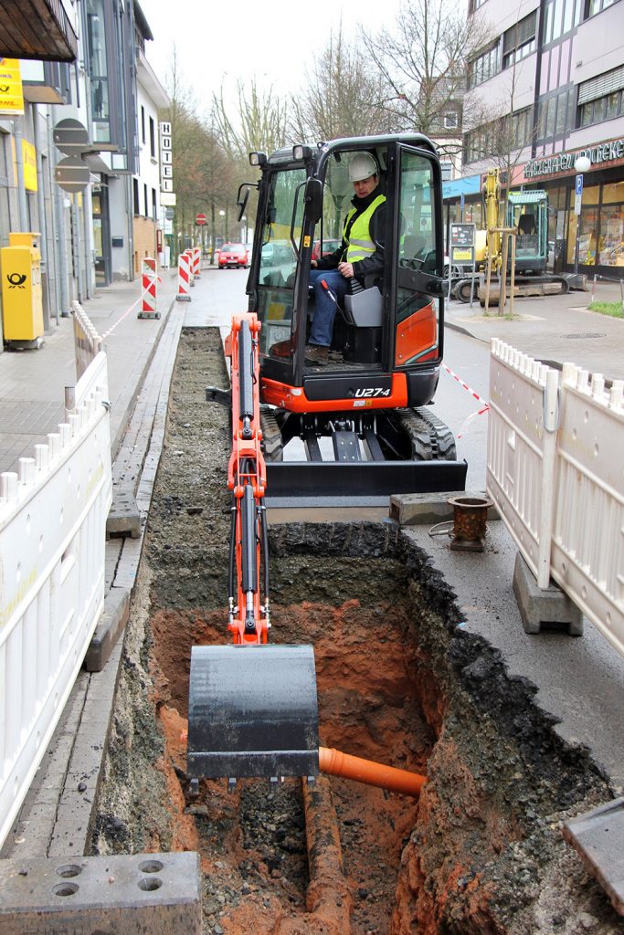 Kubota U27-4 excavator working on a local high street. Digging around a pipe in the ground. 